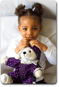young girl holding white teddy bear that is wearing a purple dress and hat