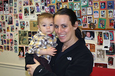 smiling Mom holding baby son in front of the wall covered with pictures