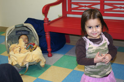 cute sis, wearing pink and green, and baby brother in front of the red bench