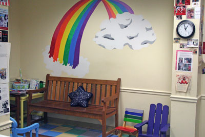 rainbow painted on wall behind bench in the waiting room, with colorful child-size chairs