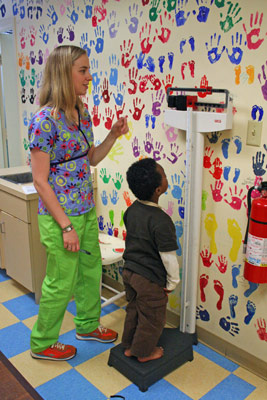 Rachel, in bright green pants and bright red shoes, weighing little Cherub